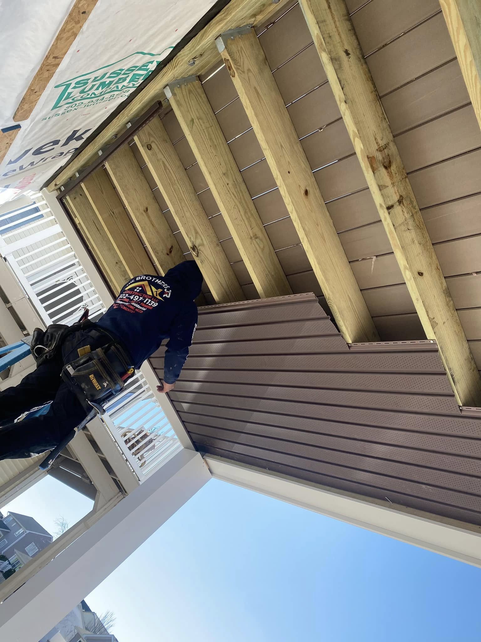 Siding installation under roof structure with worker on residential home in Lewes DE