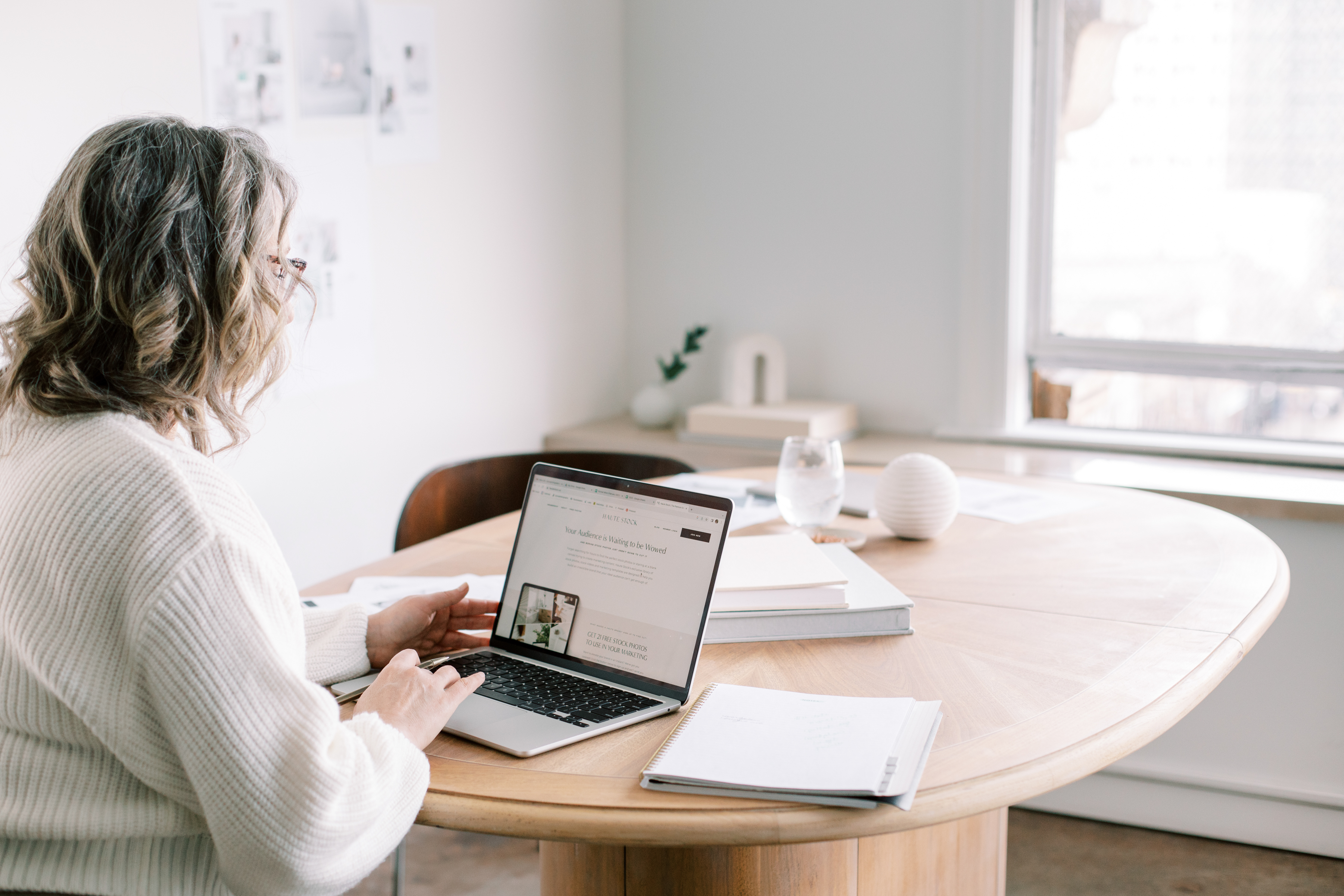 GiraffeRichMomma™ — A woman working on a laptop at a bright white table, showing a calm and simple workspace for building an online business from home.