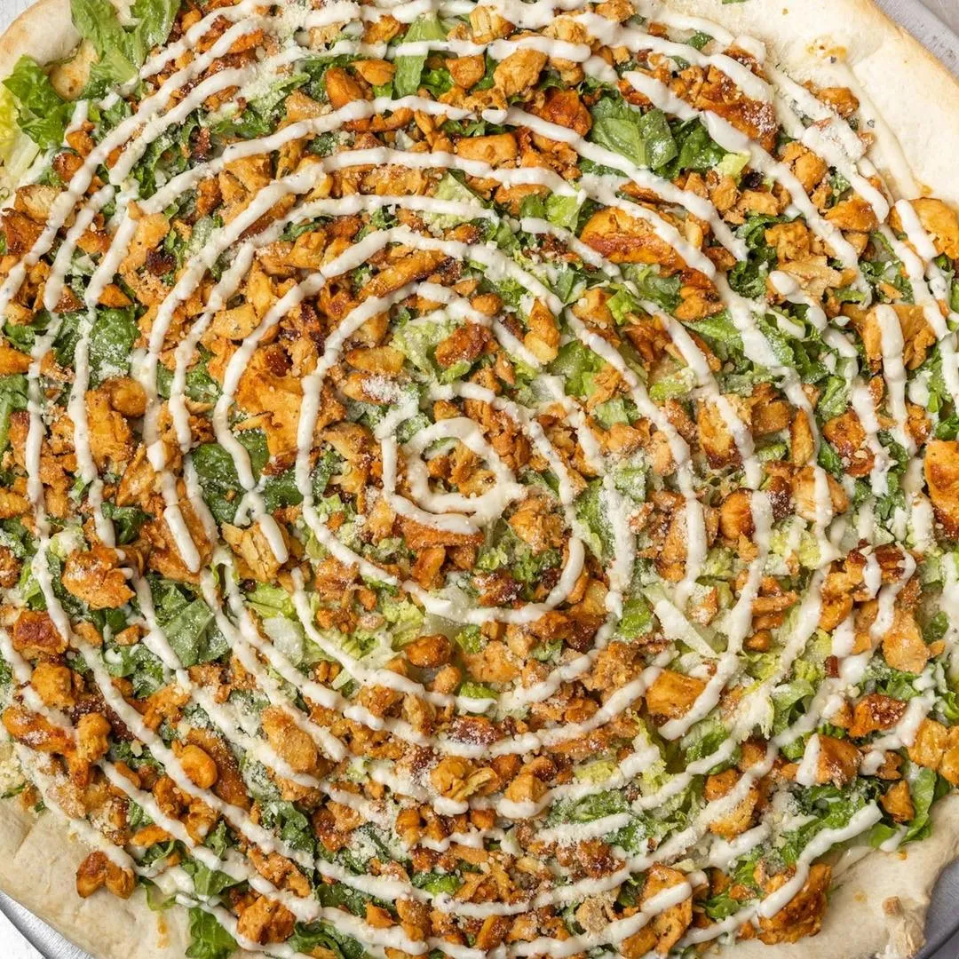 Chicken Caesar Pizza topped with grilled chicken and Caesar dressing.