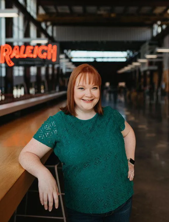 red haired woman standing at counter with Raleigh sign