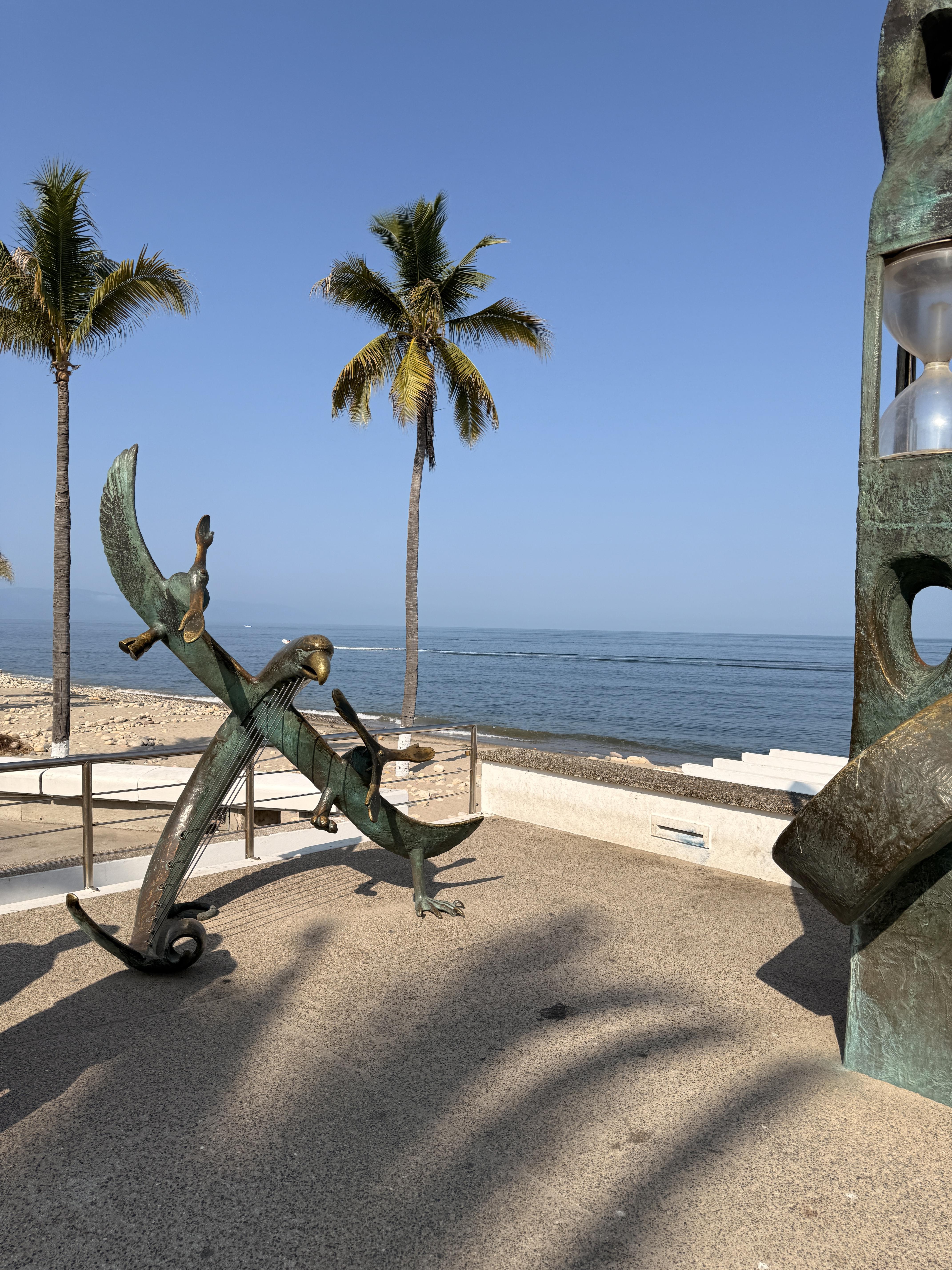 The bronze bird sculpture with outstretched wings against the backdrop of palm trees and the Pacific Ocean is simply stunning.