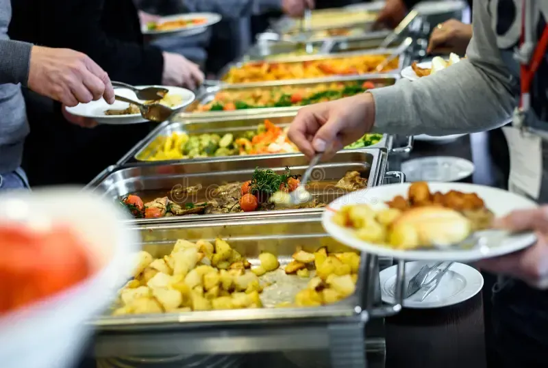A diverse family of three generations laughing together at a decorated long table, with balloons and a cake, in a sunlit restaurant space. The scene is candid, joyful, and vibrant, capturing a real moment of togetherness. 3:2 aspect ratio.