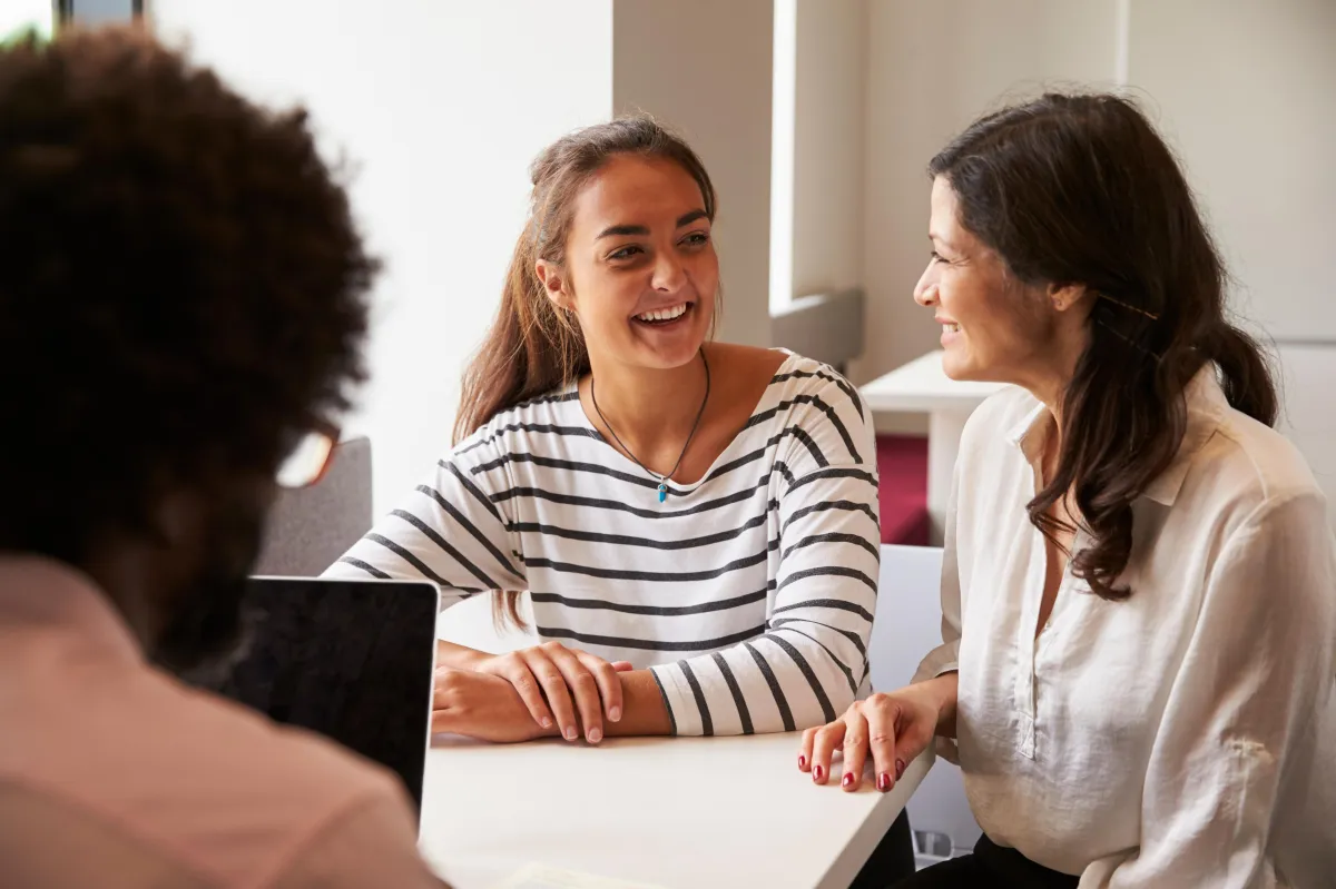 Mother and grown child laughing and talking with a third unseen person in a light office setting.