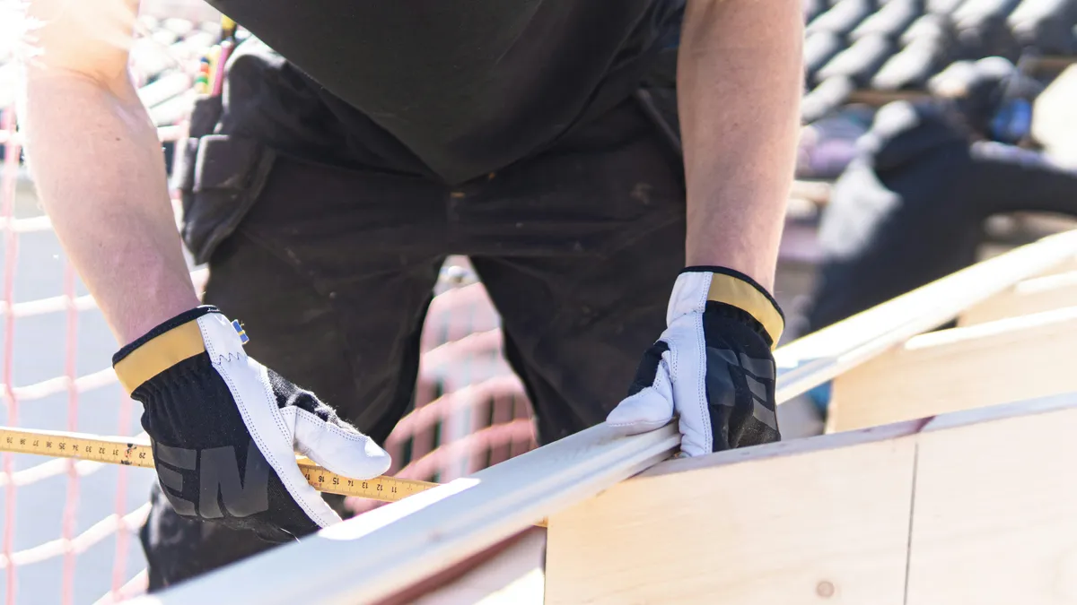 Worker measuring lumber with a tape measure during framing work