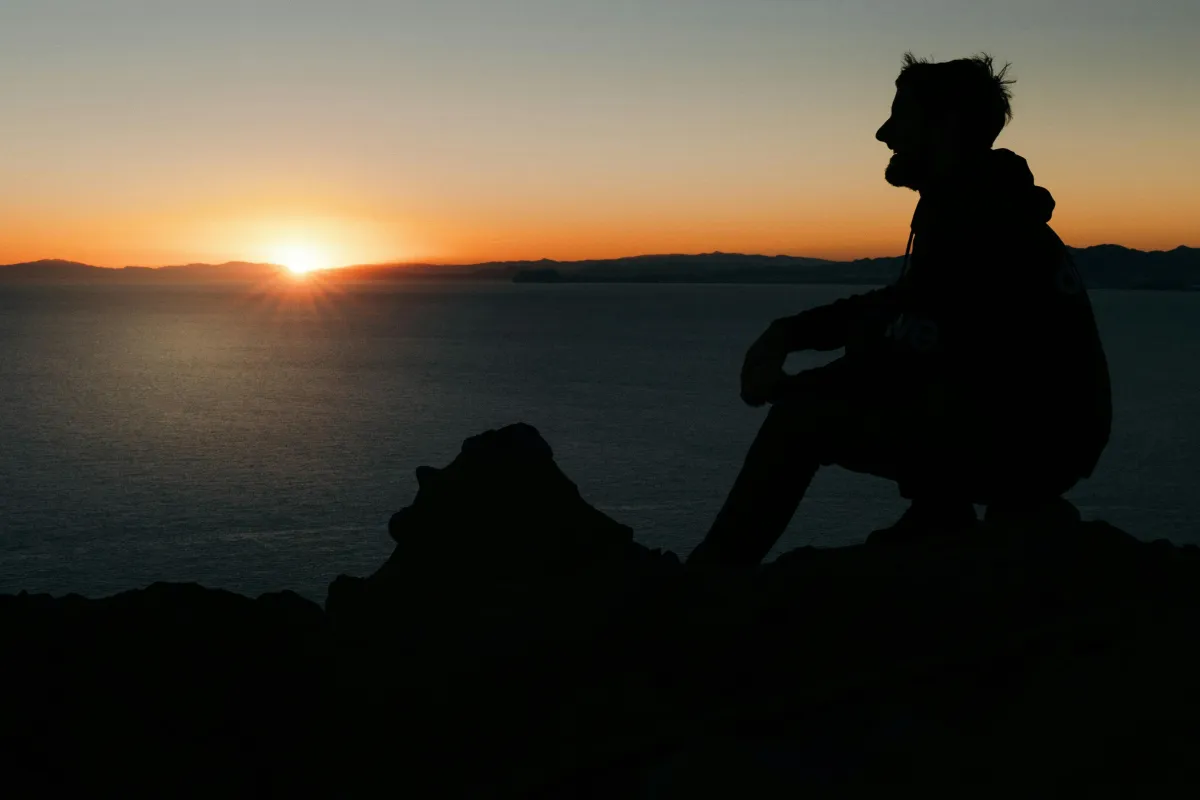 A person sits peacefully in a serene natural setting, eyes closed, practicing breathwork to calm their mind and reduce overthinking. This moment of mindfulness meditation allows them to regain control over their thoughts and emotions, promoting mental clarity and self-awareness.