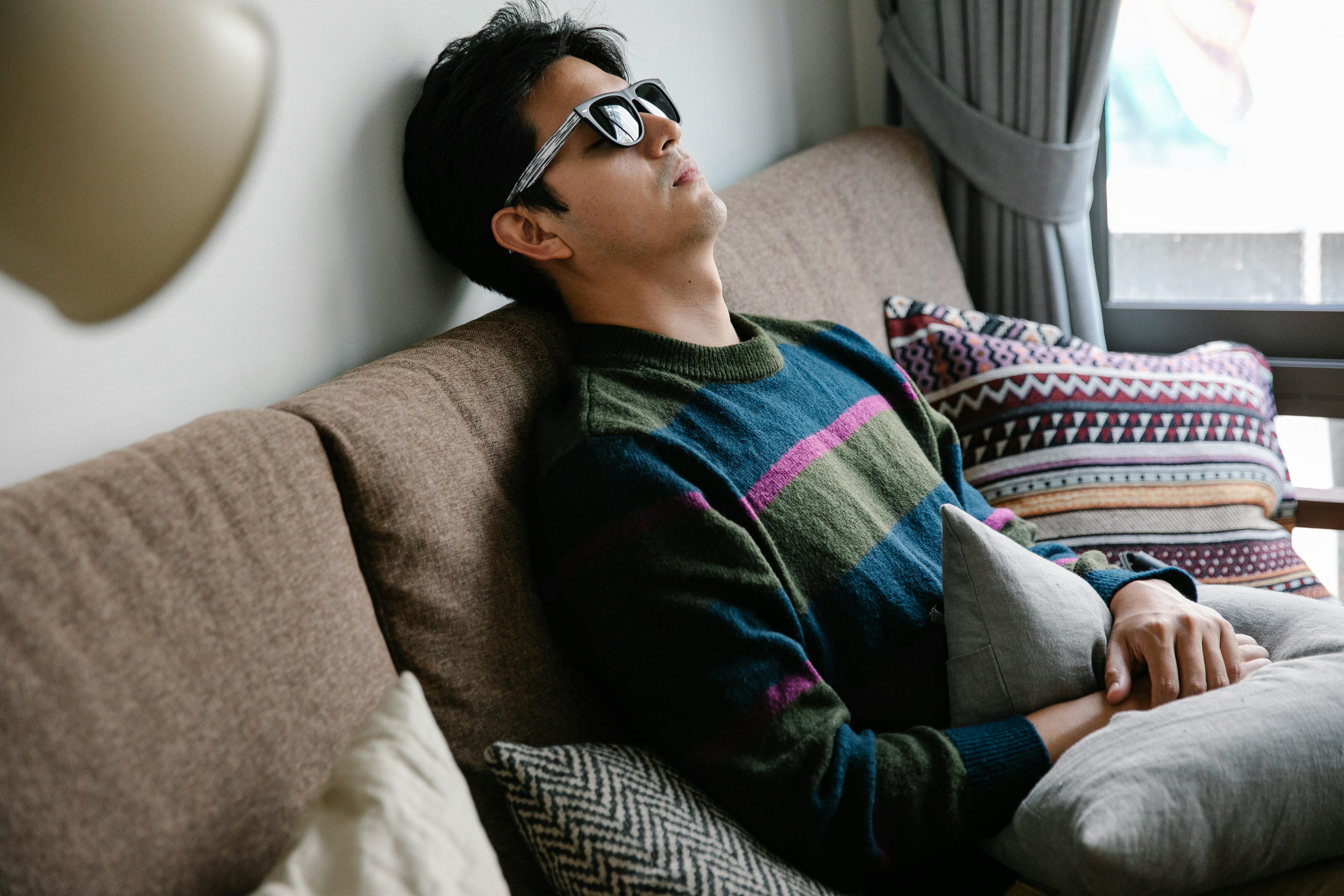 A man wearing sunglasses is reclining on a sofa, enjoying a relaxed moment indoors.