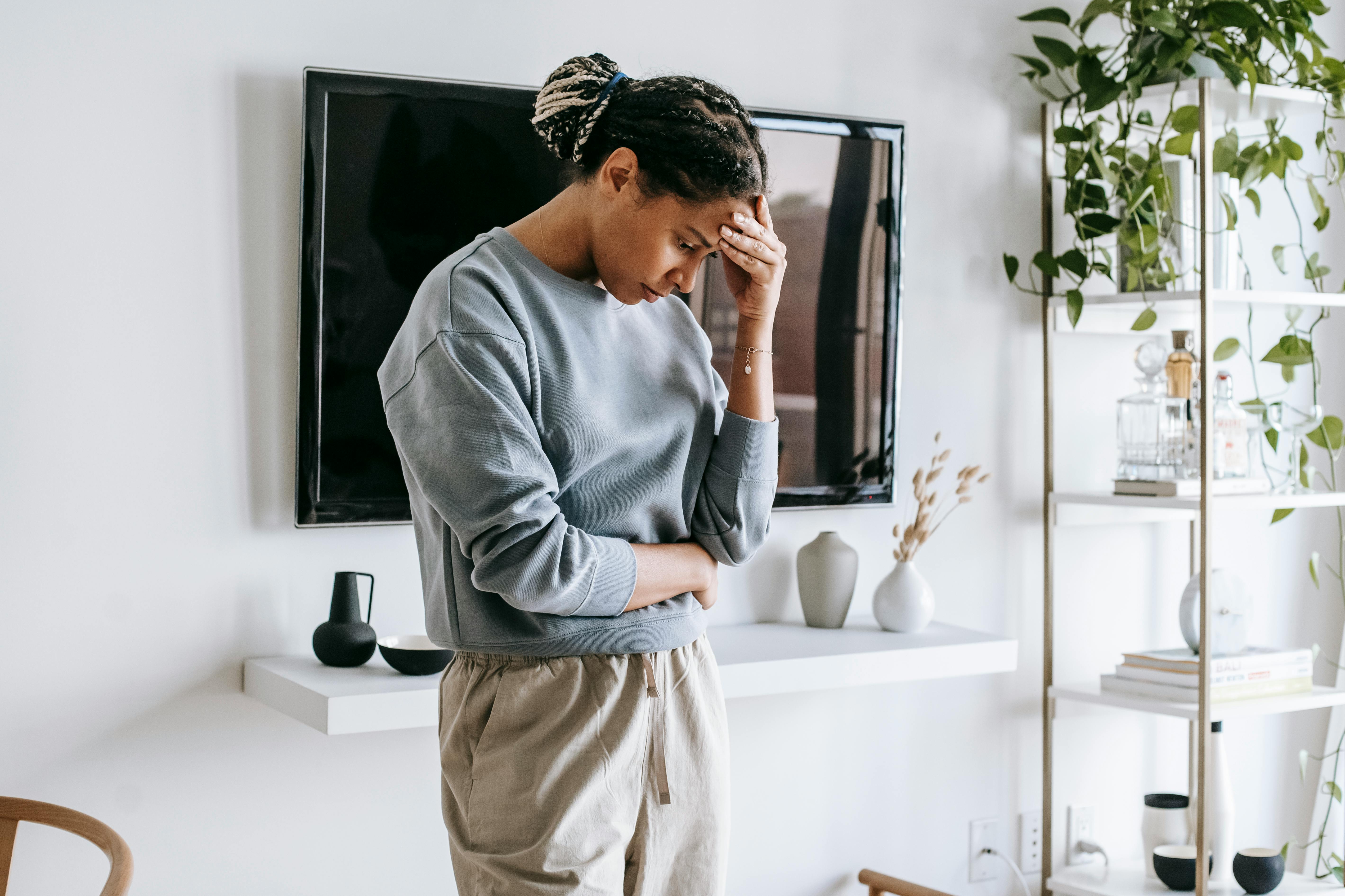 A young woman in casual attire appears deep in thought inside a modern, stylish apartment setting.