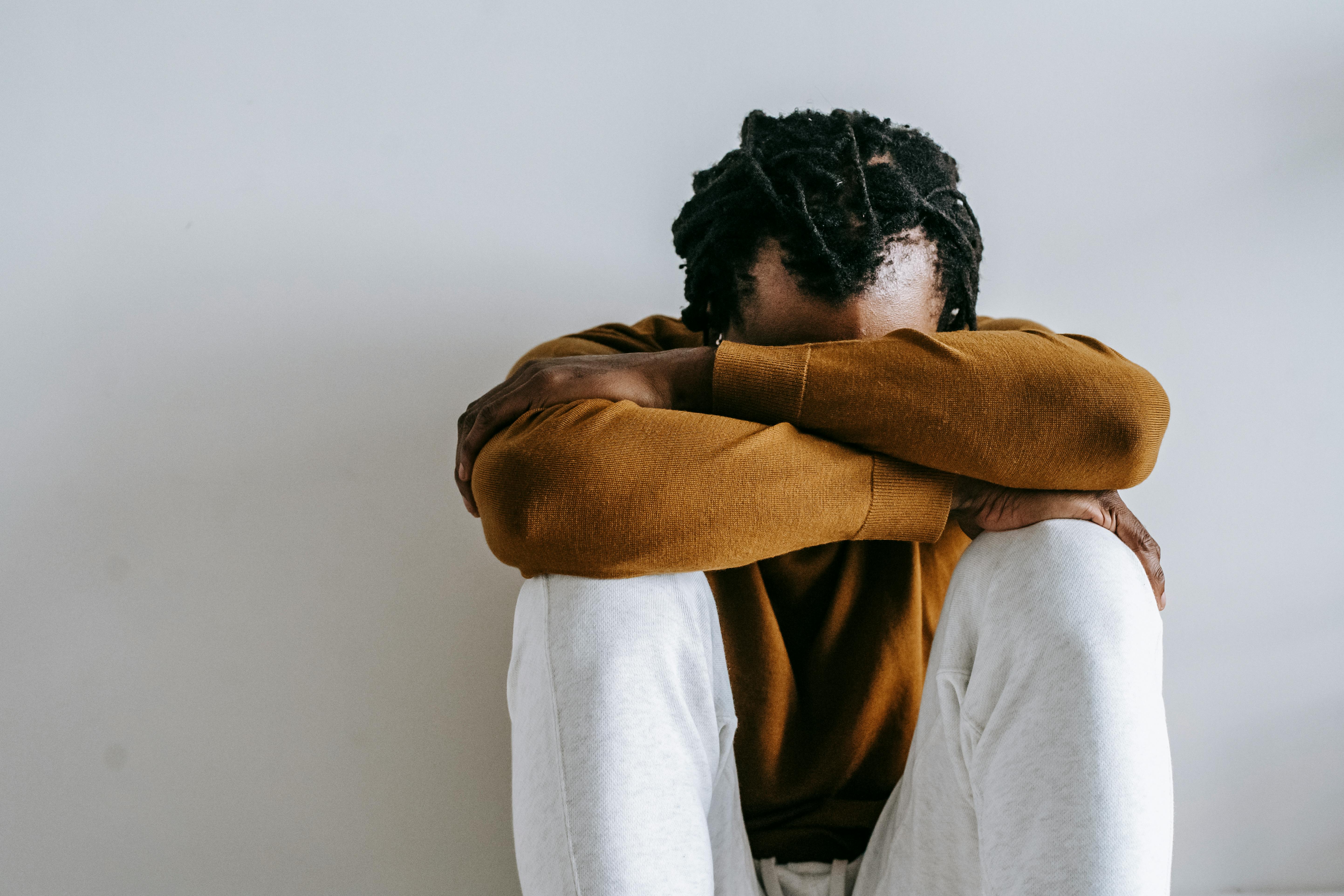 Man seated with head on knees, expressing deep emotion in a minimalist setting.