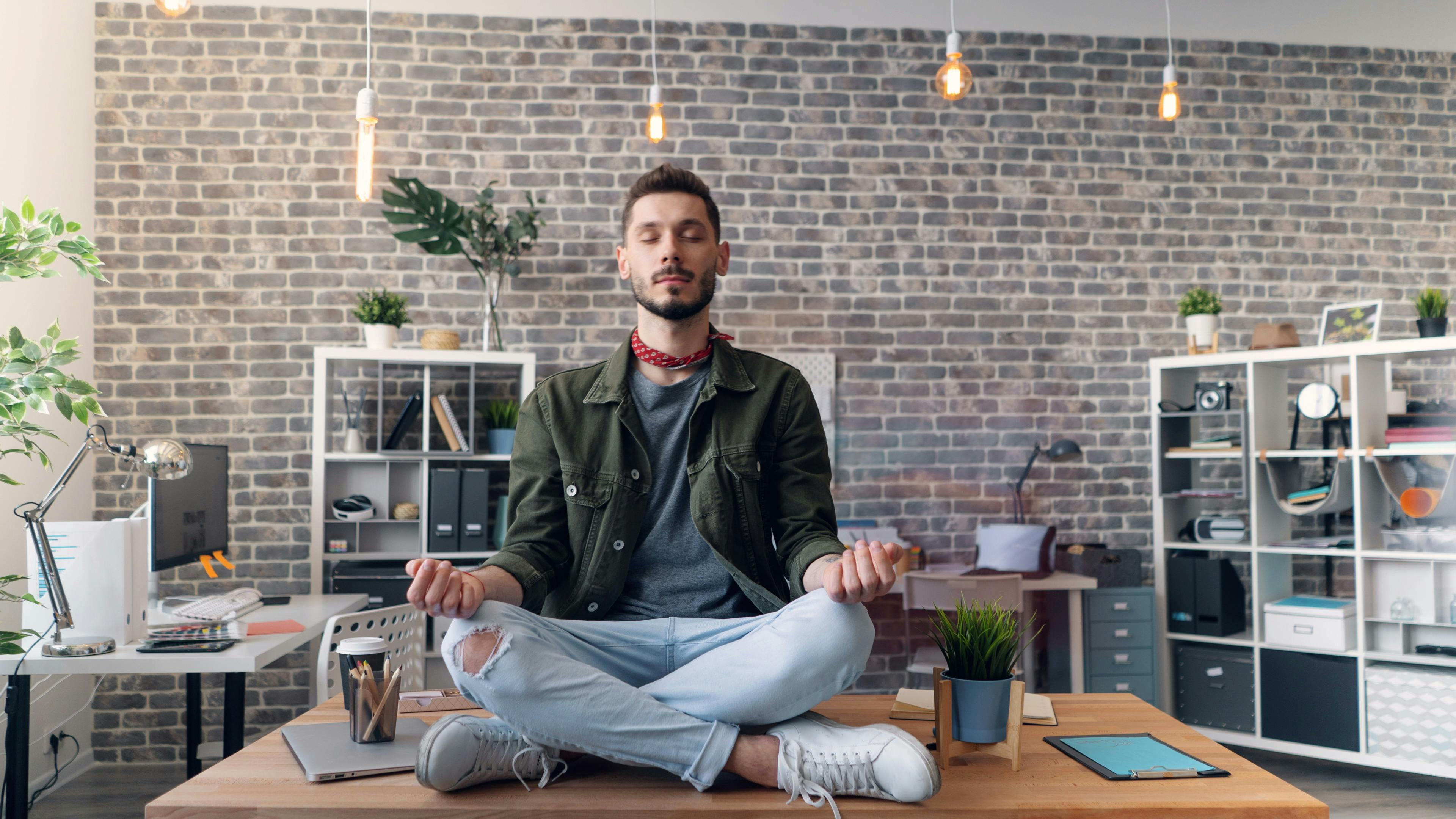 Young man practicing breathwork on a desk in a modern office with brick walls.