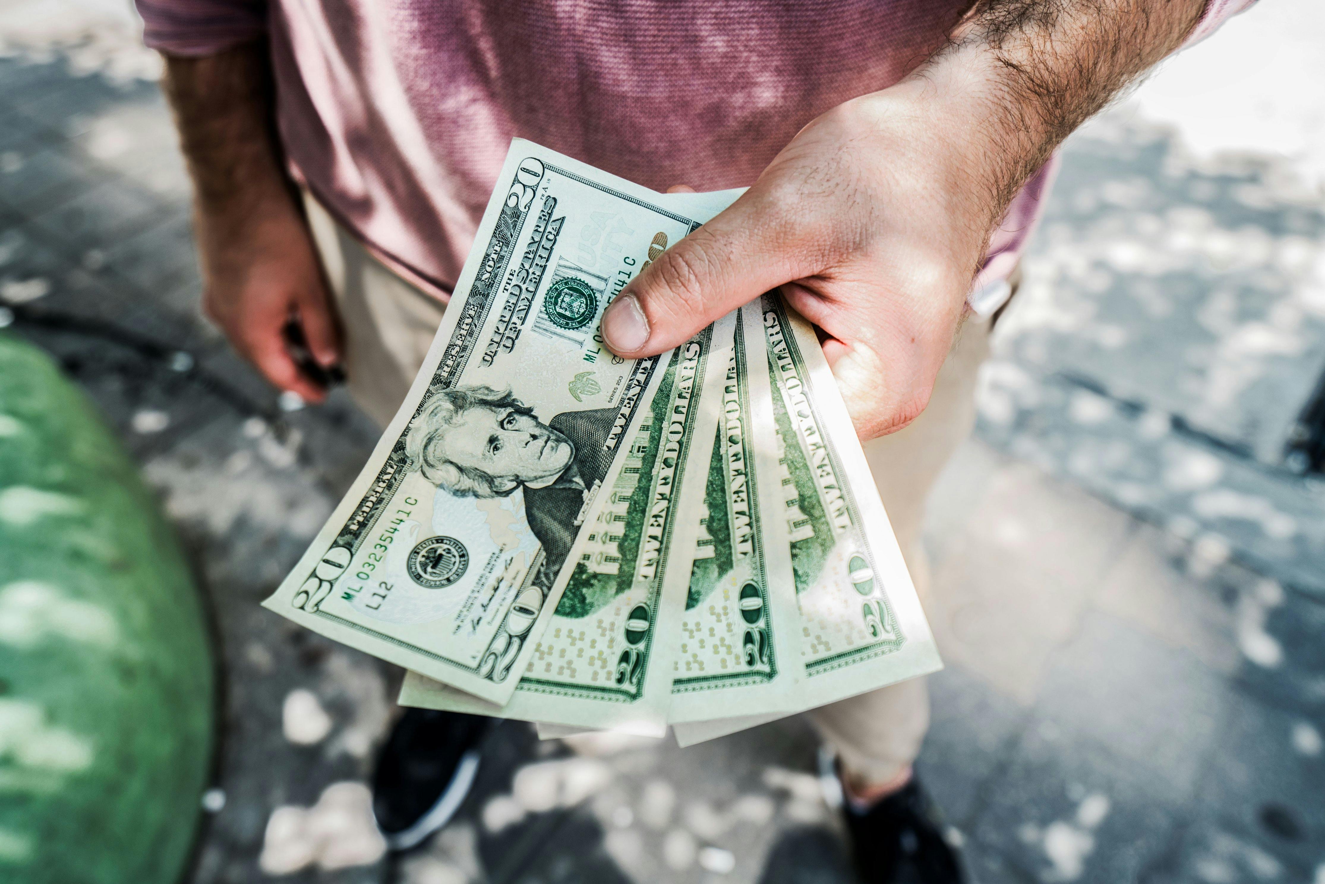 A person holding several twenty-dollar bills outdoors, depicting payment or wellness transaction.