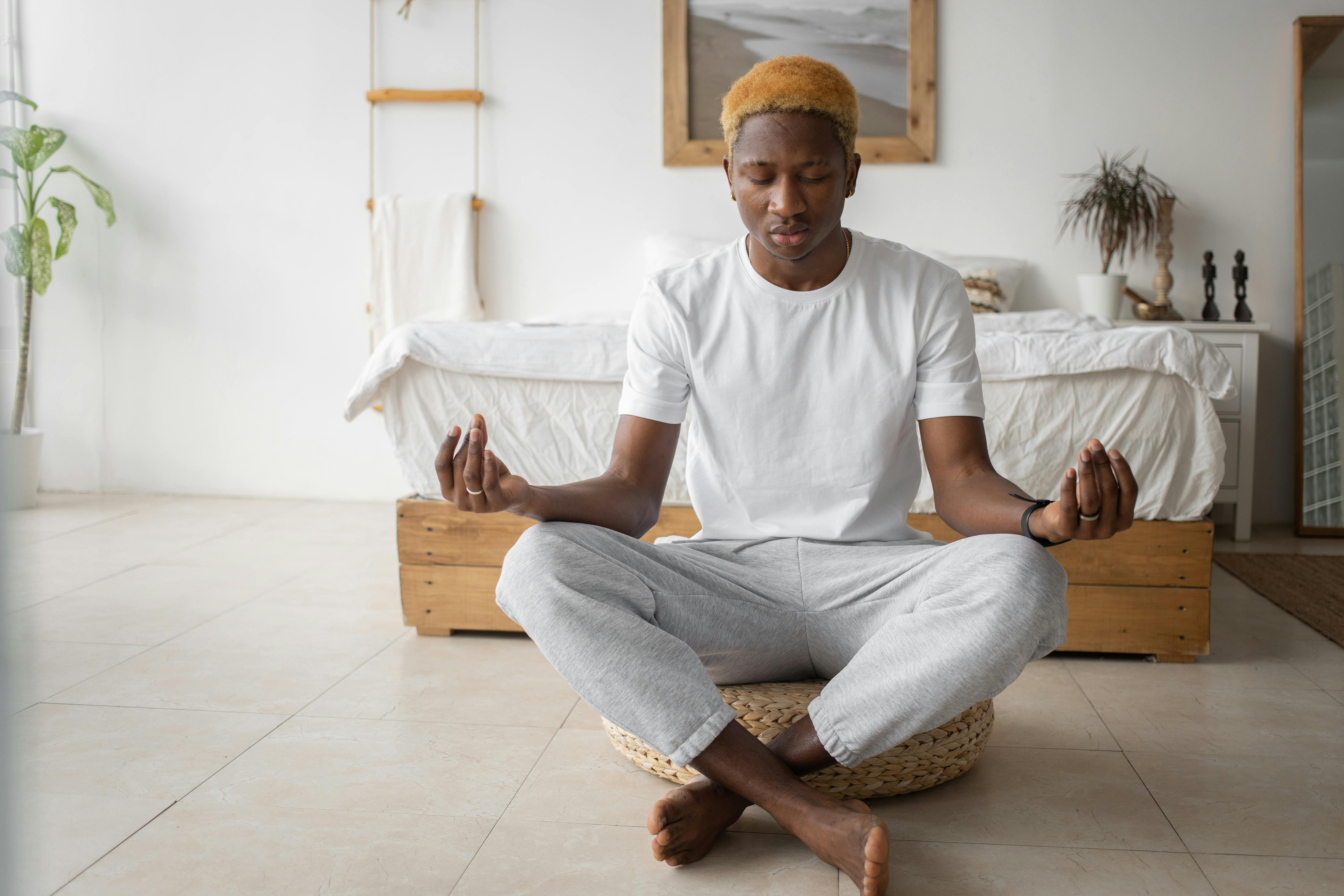 A young man practicing mindfulness meditation in a serene bedroom setting.