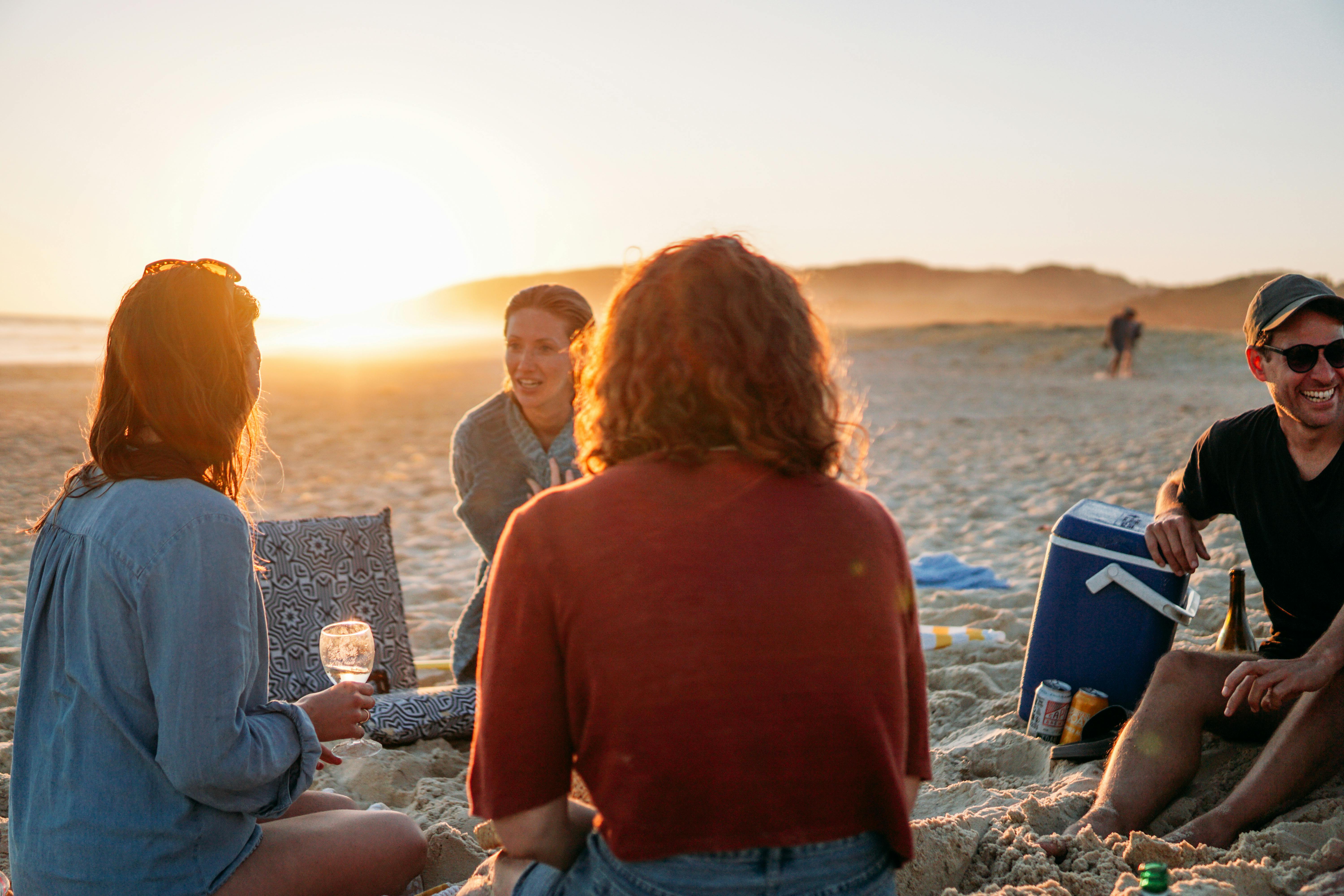 Group of friends relaxing on a beach during a beautiful sunset, enjoying drinks and good company.