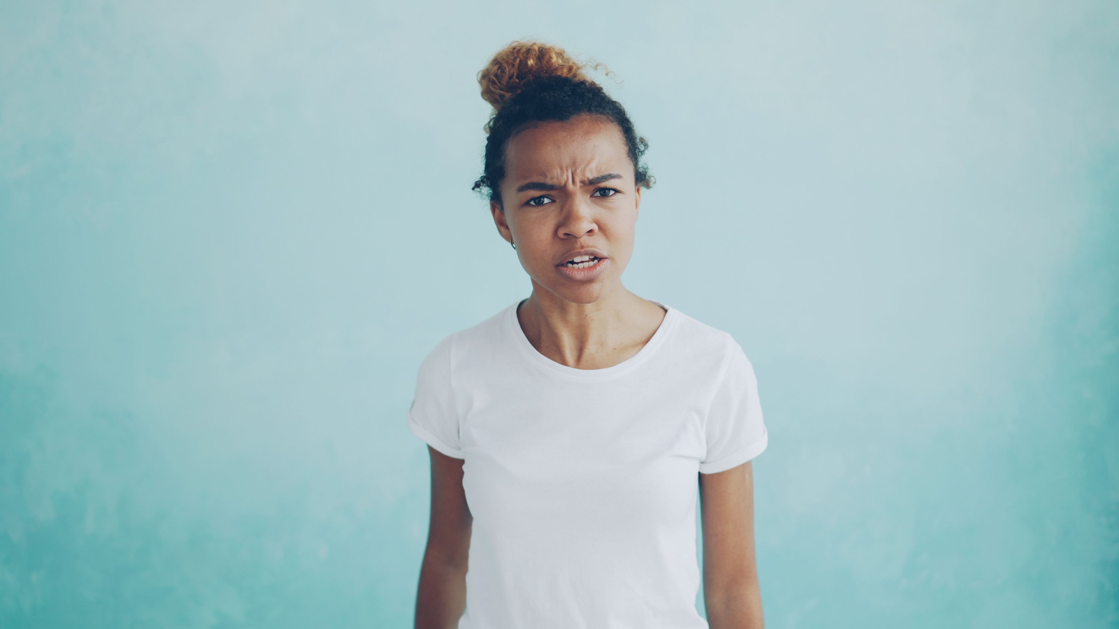 Portrait of a woman in a white t-shirt expressing anger against a blue background.