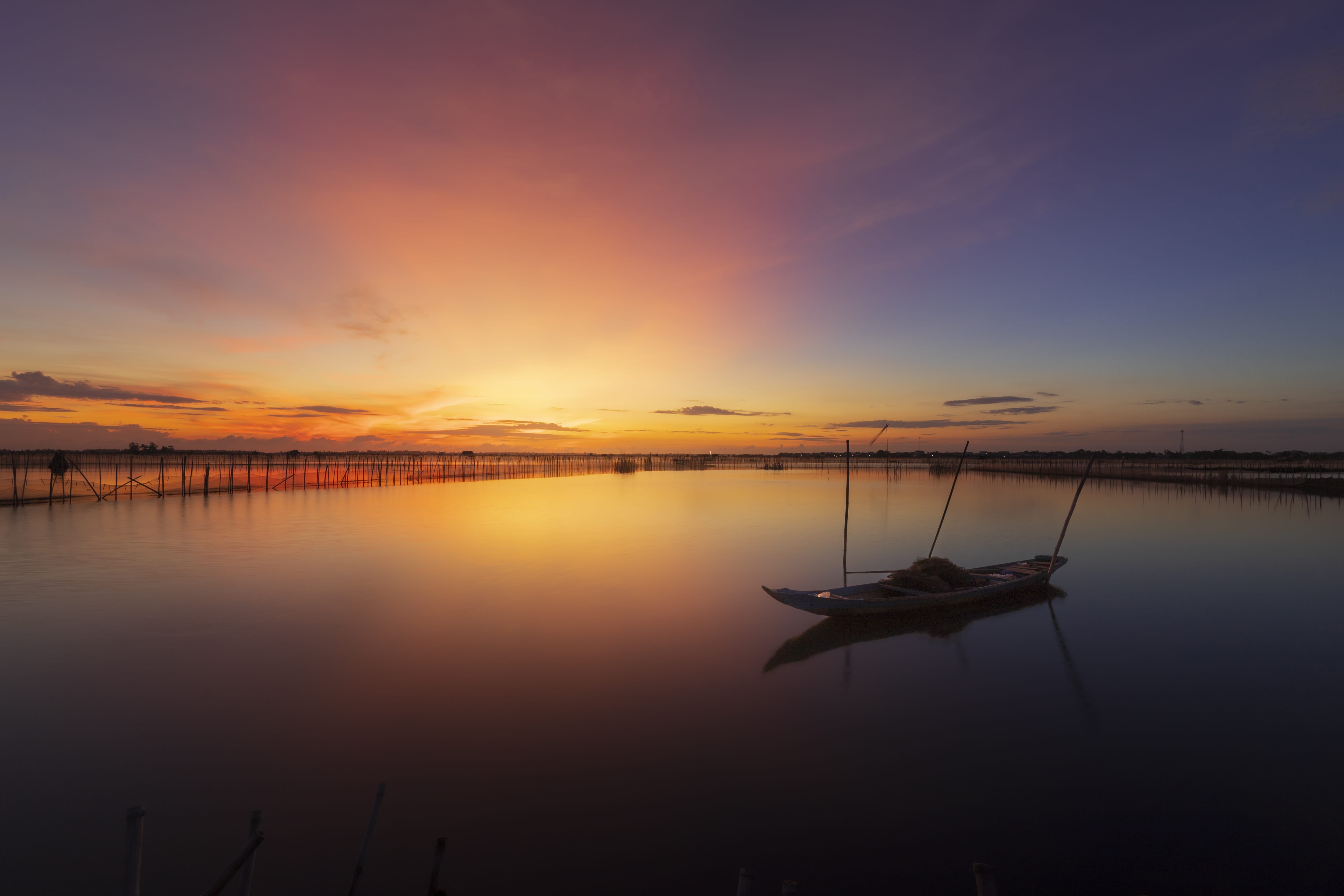 Serene lake sunset with a lone boat reflecting colorful skies and calm waters relaxing for nervous system regulation