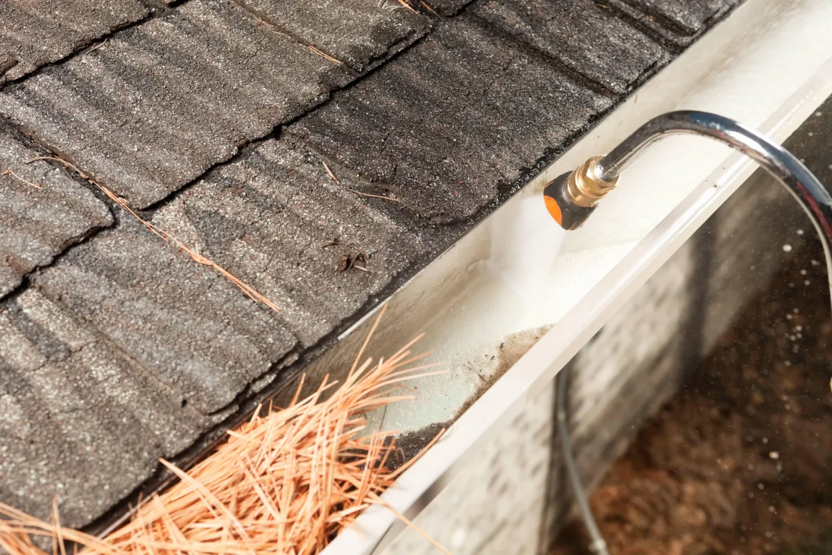 Pressure washing dirty gutters filled with pine needles and the gutters are attached to a house in Albany GA