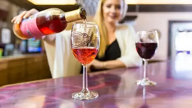 Person pouring rosé wine into a glass, showcasing bar ambiance.