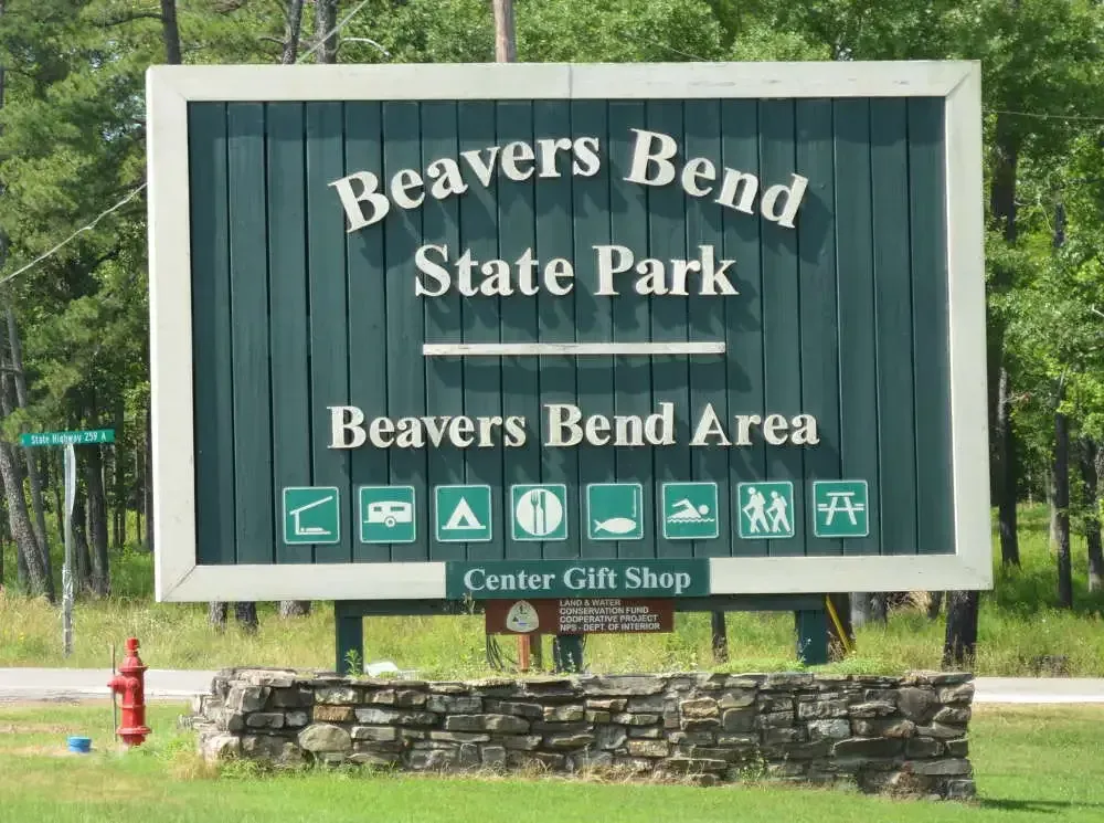 Wooden park sign with activity icons, stone base, and scenic backdrop.
