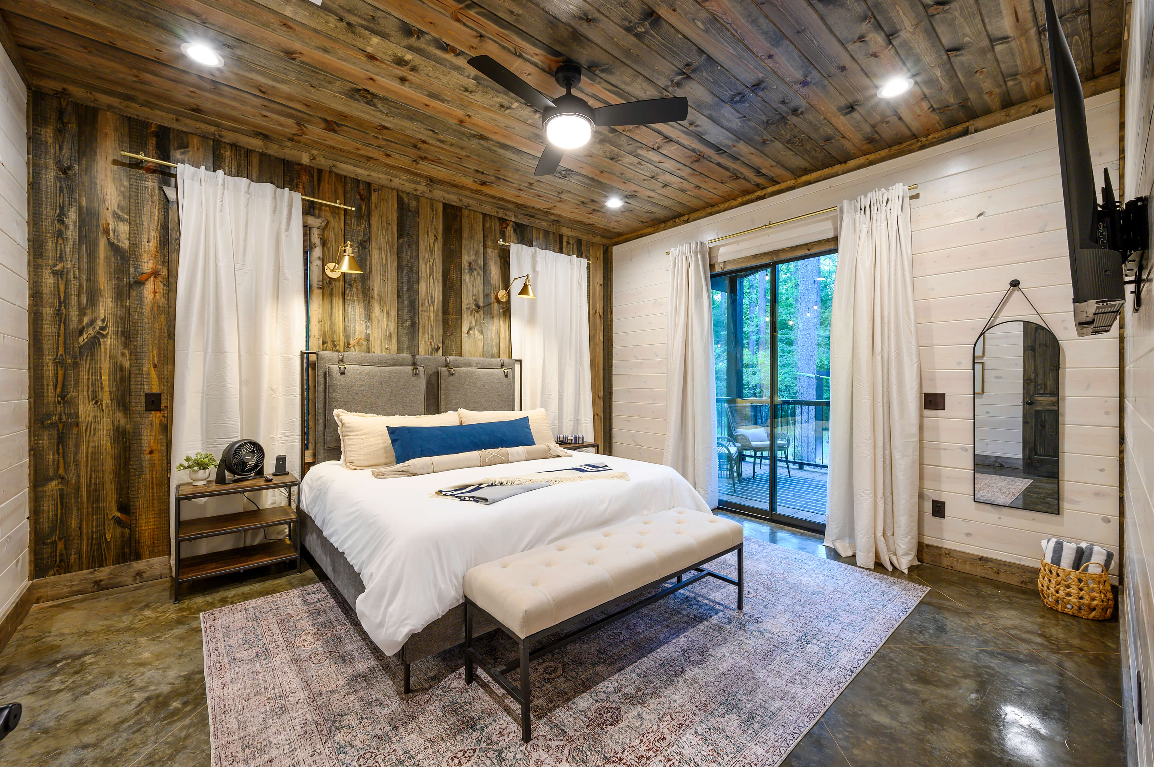 Rustic bedroom with wooden ceiling, blue accents, and large windows to nature.