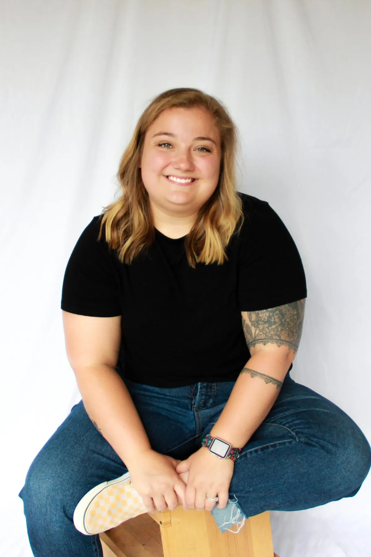 Happy headshot of Cara Wallskog the owner of Sunny Lane Marketing sitting against a white backdrop with a black shirt and yellow shoes.