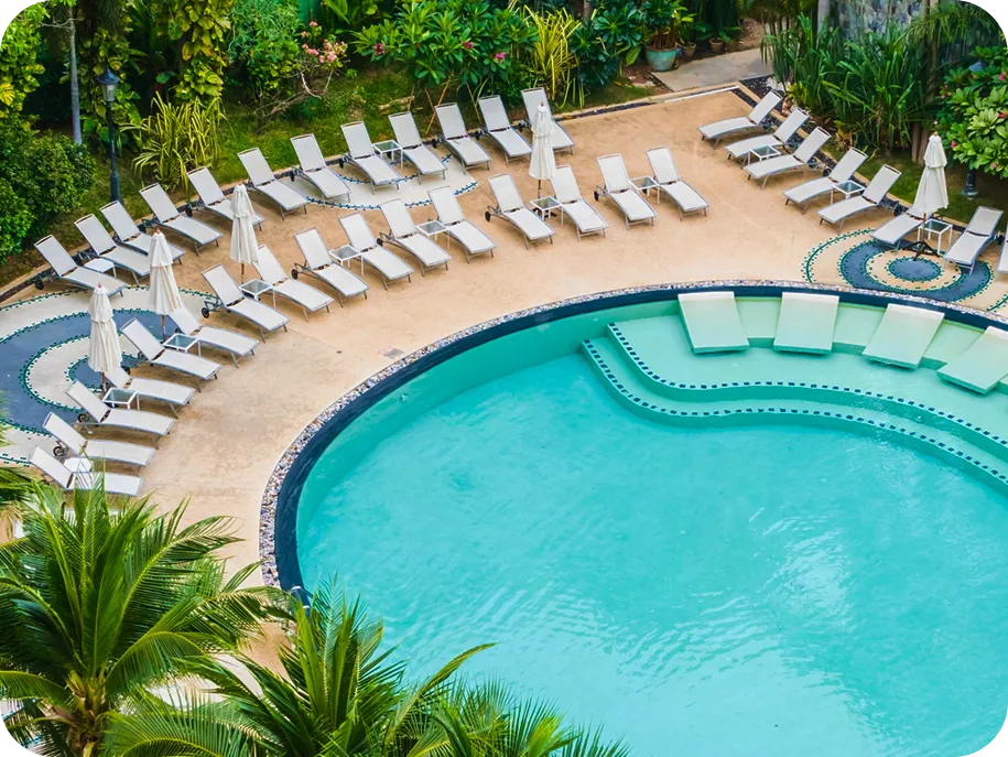 Overhead view of a resort-style pool surrounded by white lounge chairs and tropical landscaping.