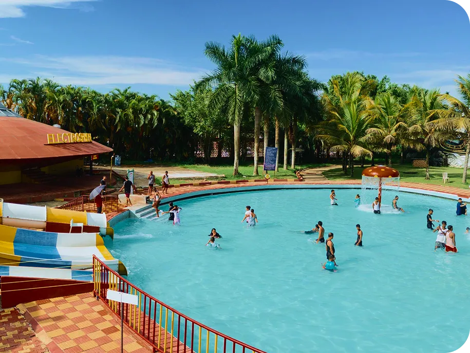 Families and children enjoying a waterpark pool with slides, palm trees, and interactive water features.