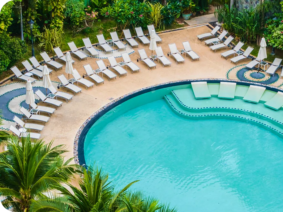 Overhead view of a resort-style pool surrounded by white lounge chairs and tropical landscaping.
