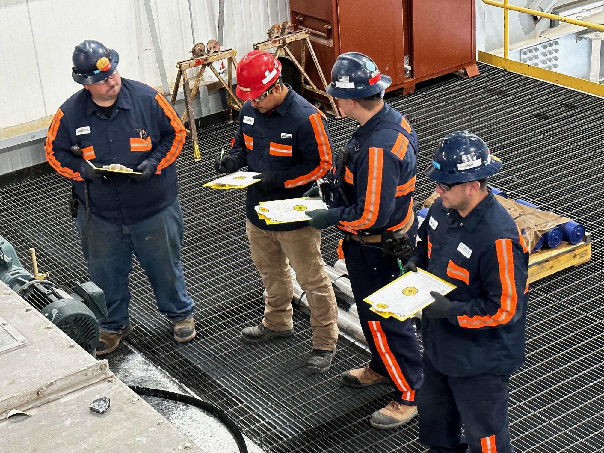 Team of workers in safety gear reviewing hazard recognition checklist during on-site HRP coaching session