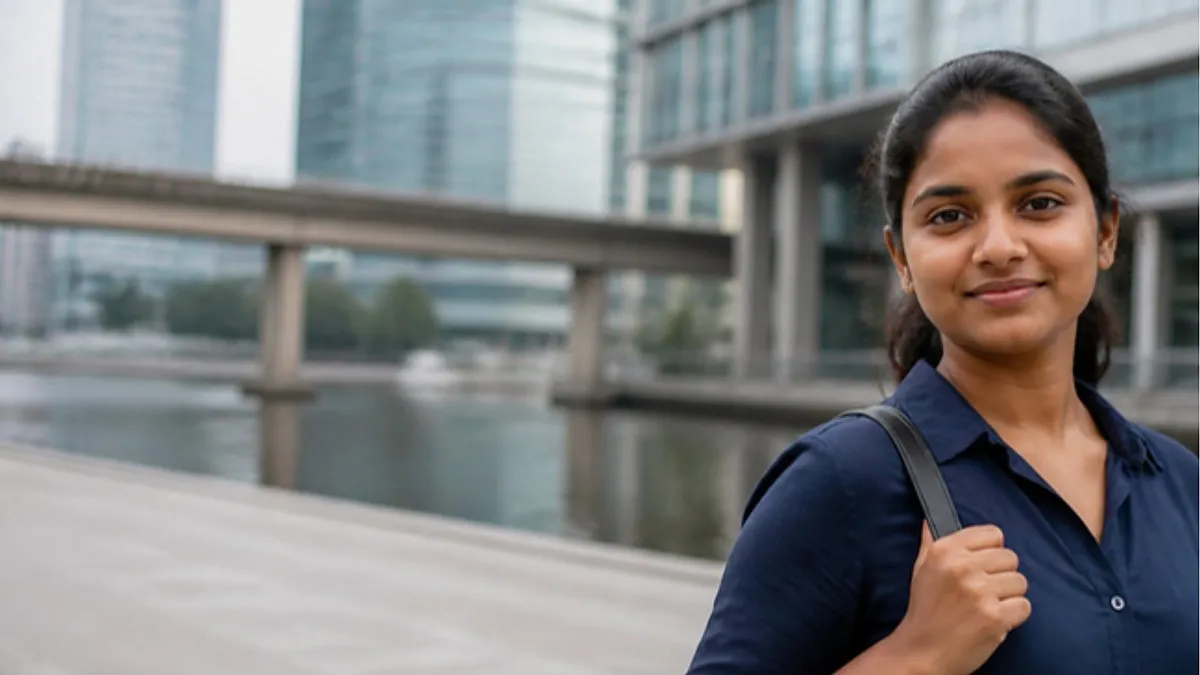 A young woman in a navy shirt stands by the dock water on a modern London Docklands campus, considering the University of East London.