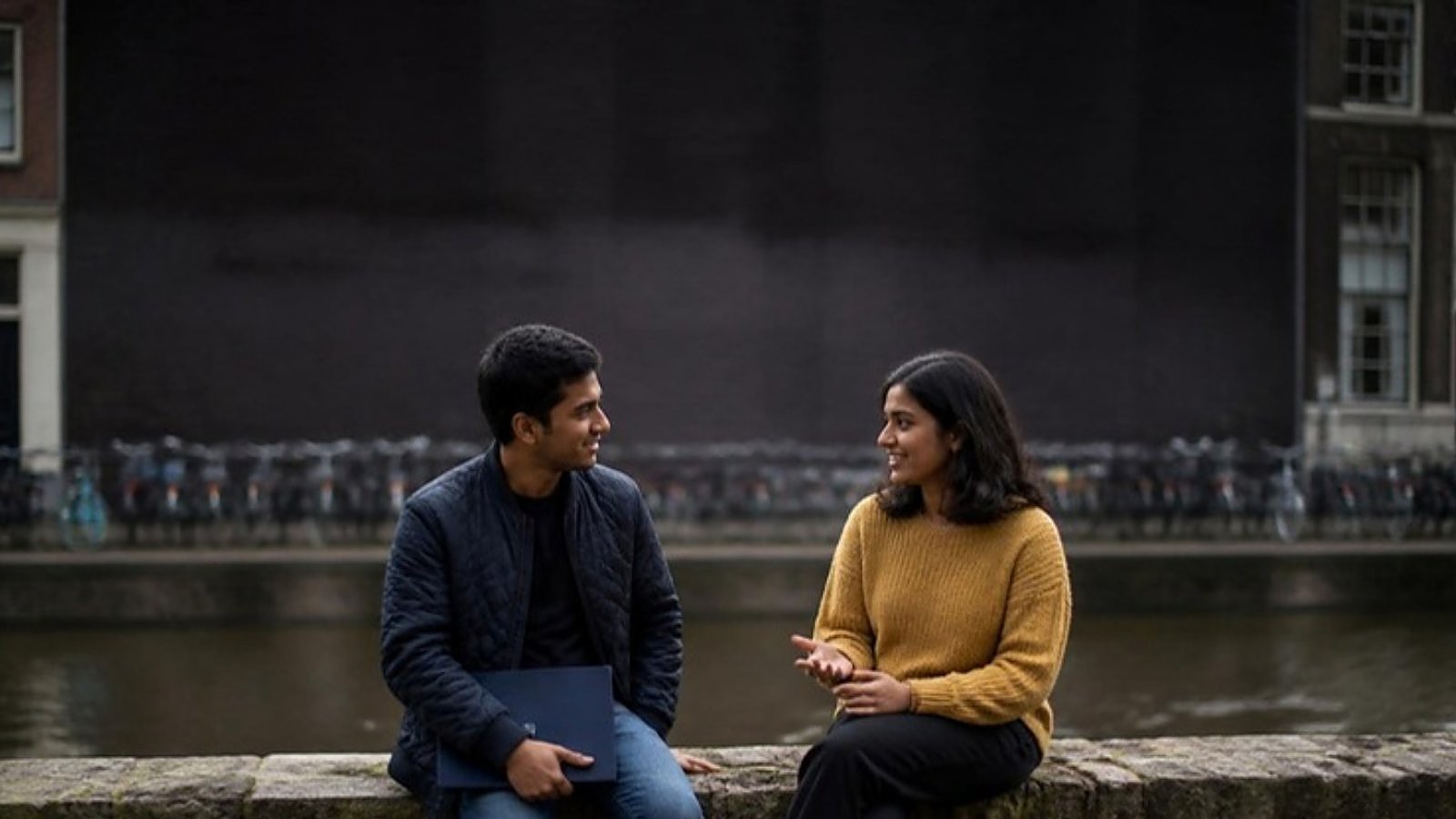 Two students talk on a canal wall in a Dutch city, comparing a research university vs university of applied sciences in the Netherlands.