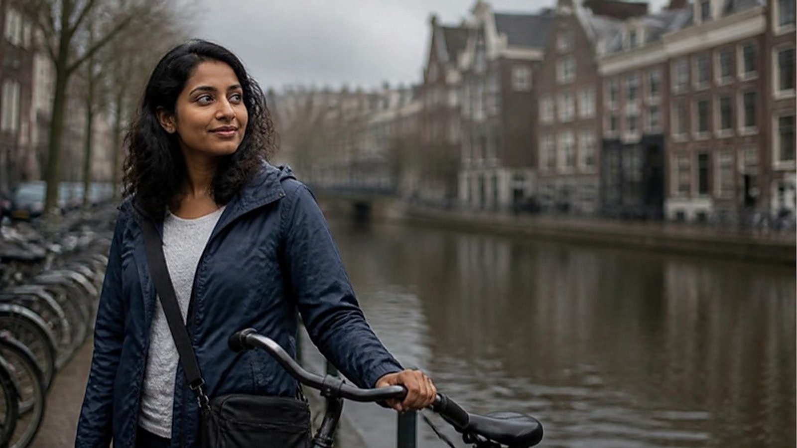A student in a navy rain jacket rests a hand on her bicycle beside a Dutch canal, weighing Netherlands tuition fees for non-EU students.