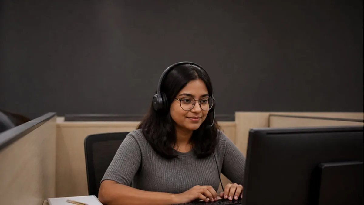 A student wearing a headset types an answer in a partitioned booth at a computer-based test centre while sitting the PTE exam.