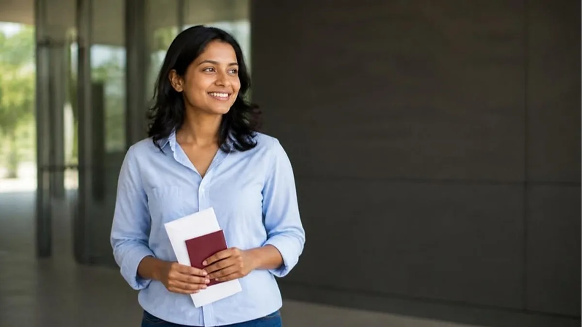 A Sri Lankan student in a light blue shirt smiles in a building corridor holding her passport and papers, ready for her IOM Colombo TB screening for a UK visa.