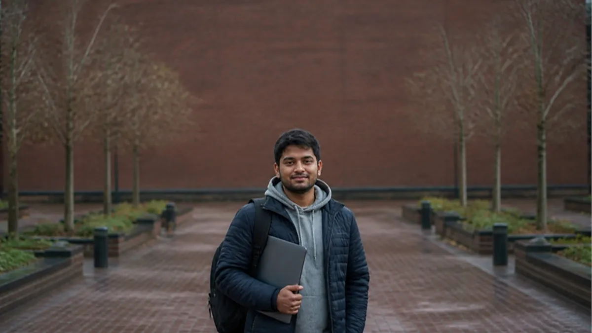 A student with a backpack and laptop stands on a red-brick UK campus walkway in autumn, the kind of campus setting found at Teesside University.