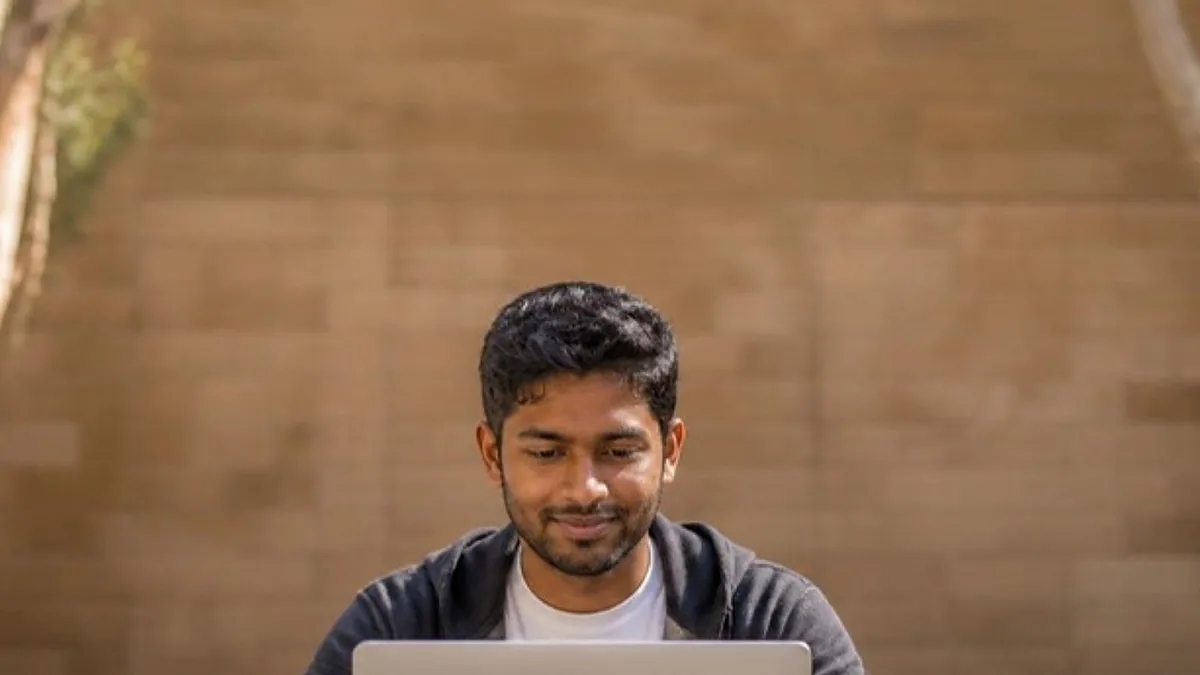 A postgraduate student types on a laptop at a stone table beside a sandstone wall on an Australian university campus, comparing a master of cyber security in Australia.