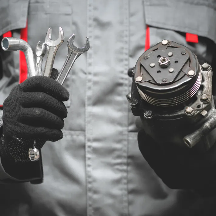 Mechanic holding wrenches and automotive part, ready for vehicle repair or maintenance.