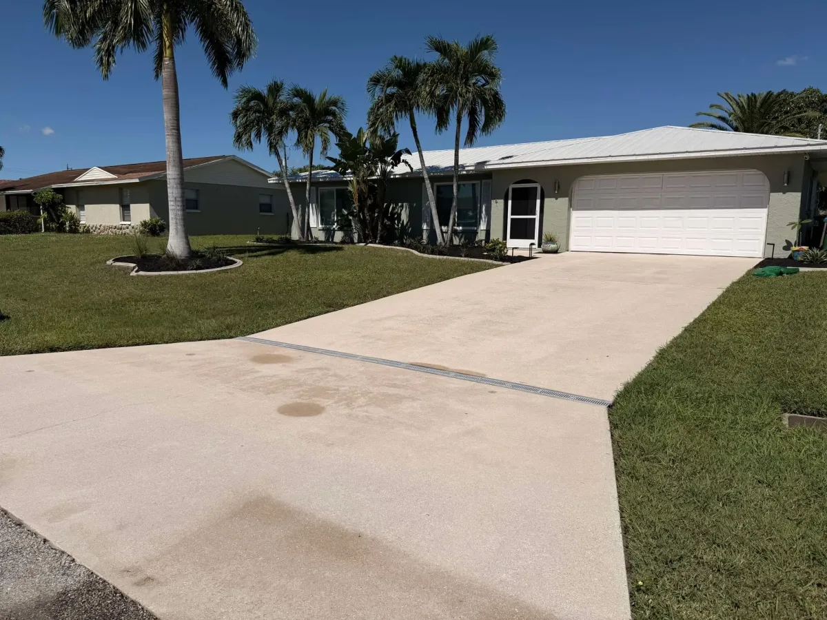 Residential driveway before pressure washing, showing visible stains and discoloration in front of a single-story home with palm trees in Cape Coral, Florida.