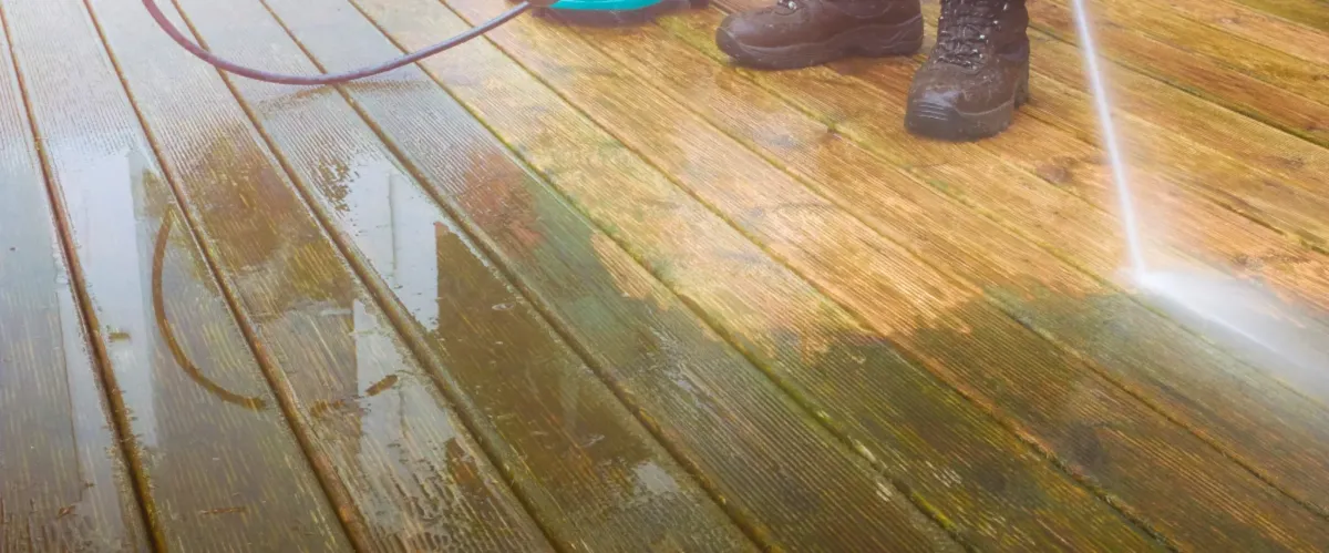 Pressure washing a wooden deck to remove dirt and algae buildup.