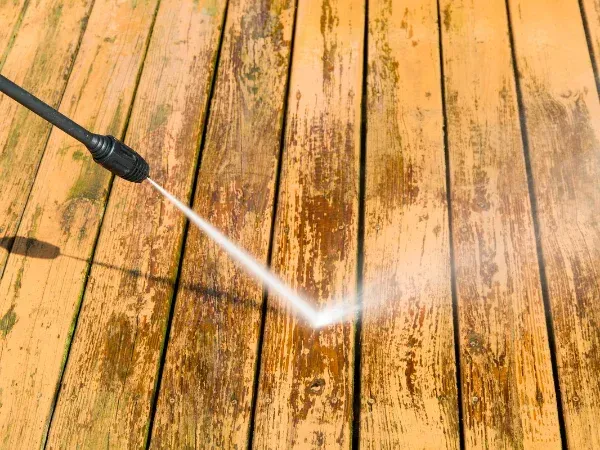 Pressure washing a weathered wooden deck to remove dirt and restore the wood surface.