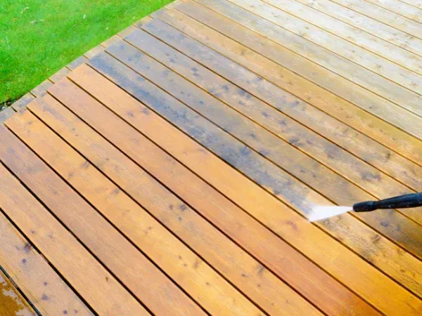 Power washer cleaning a residential wooden deck with visible clean and dirty sections.