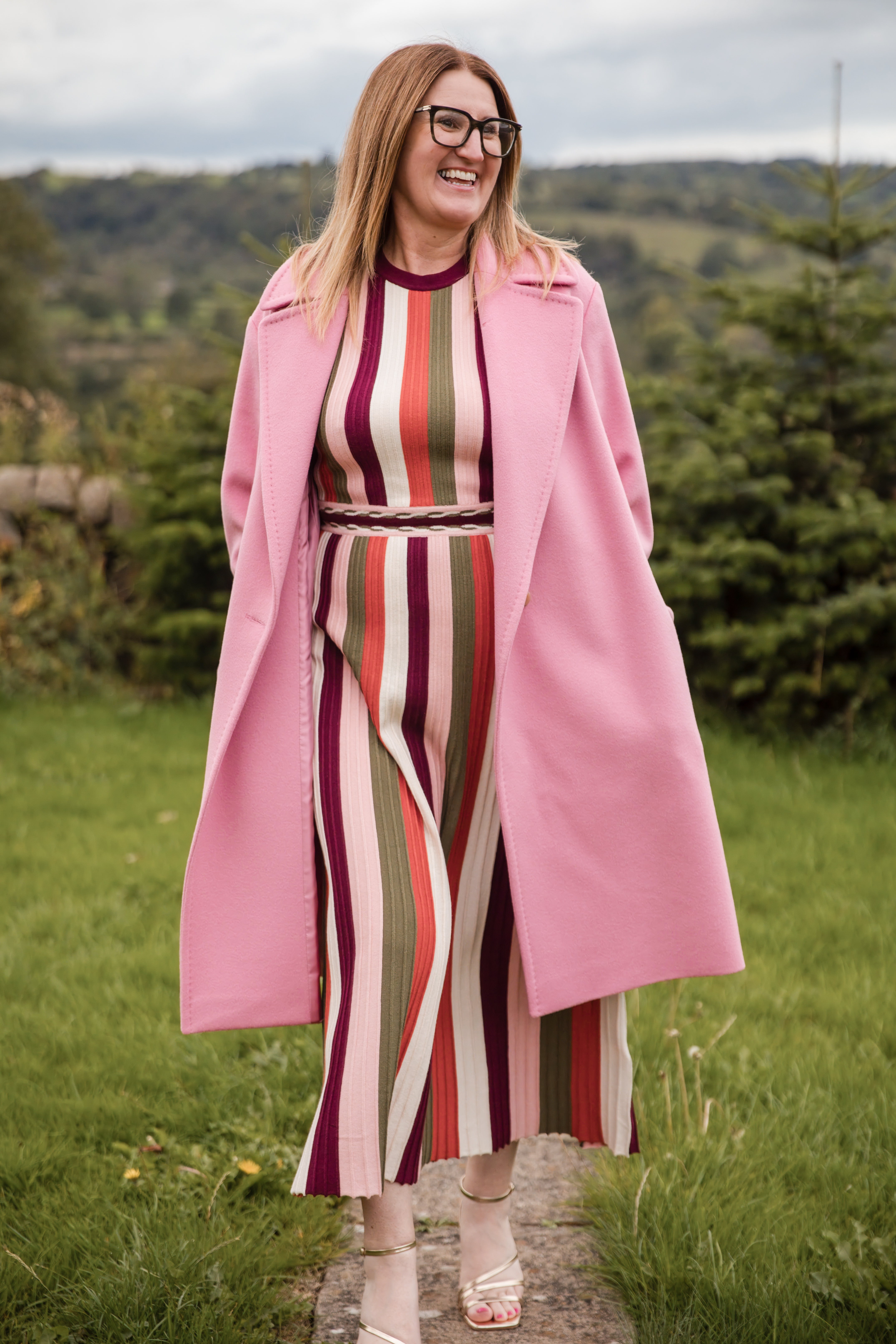Emma Hine, a woman wearing glasses, a long striped dress and pink coat.