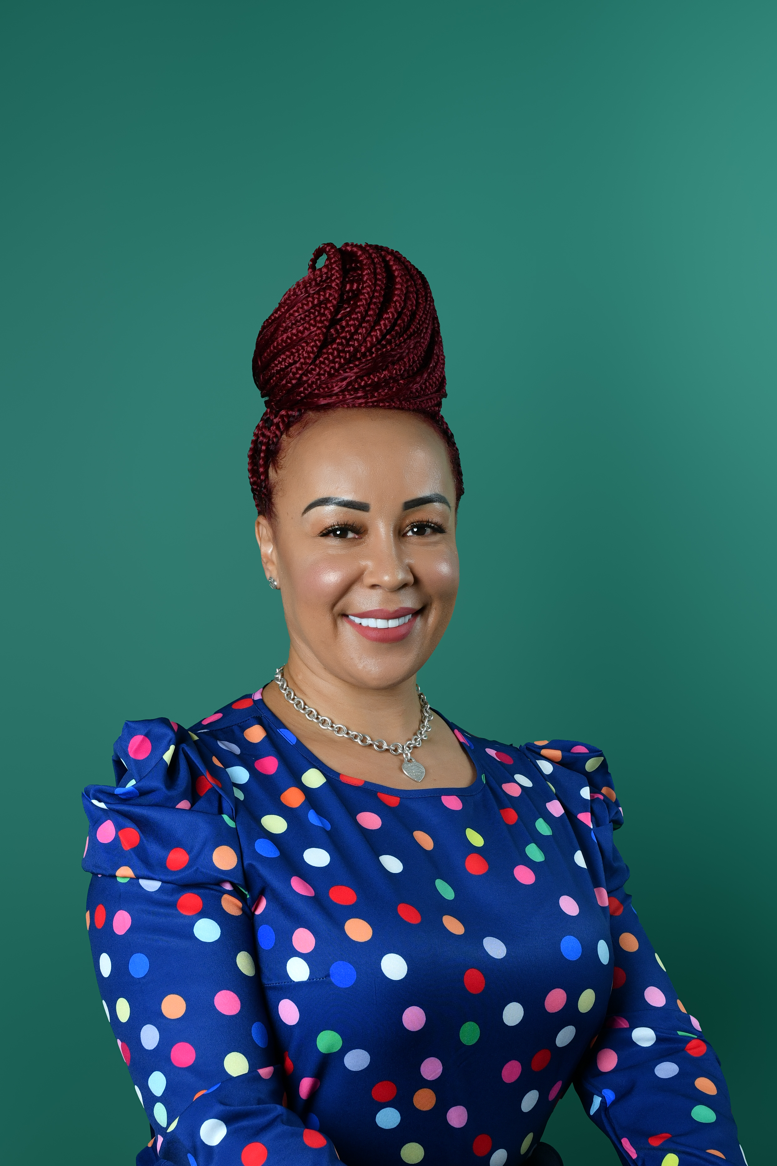 Portrait of Coach Maya Roberts, a Black woman in her 50s with silver-streaked locs, wearing a tailored black suit, seated in a modern chair. Her poised demeanor and gentle smile radiate wisdom and encouragement.
