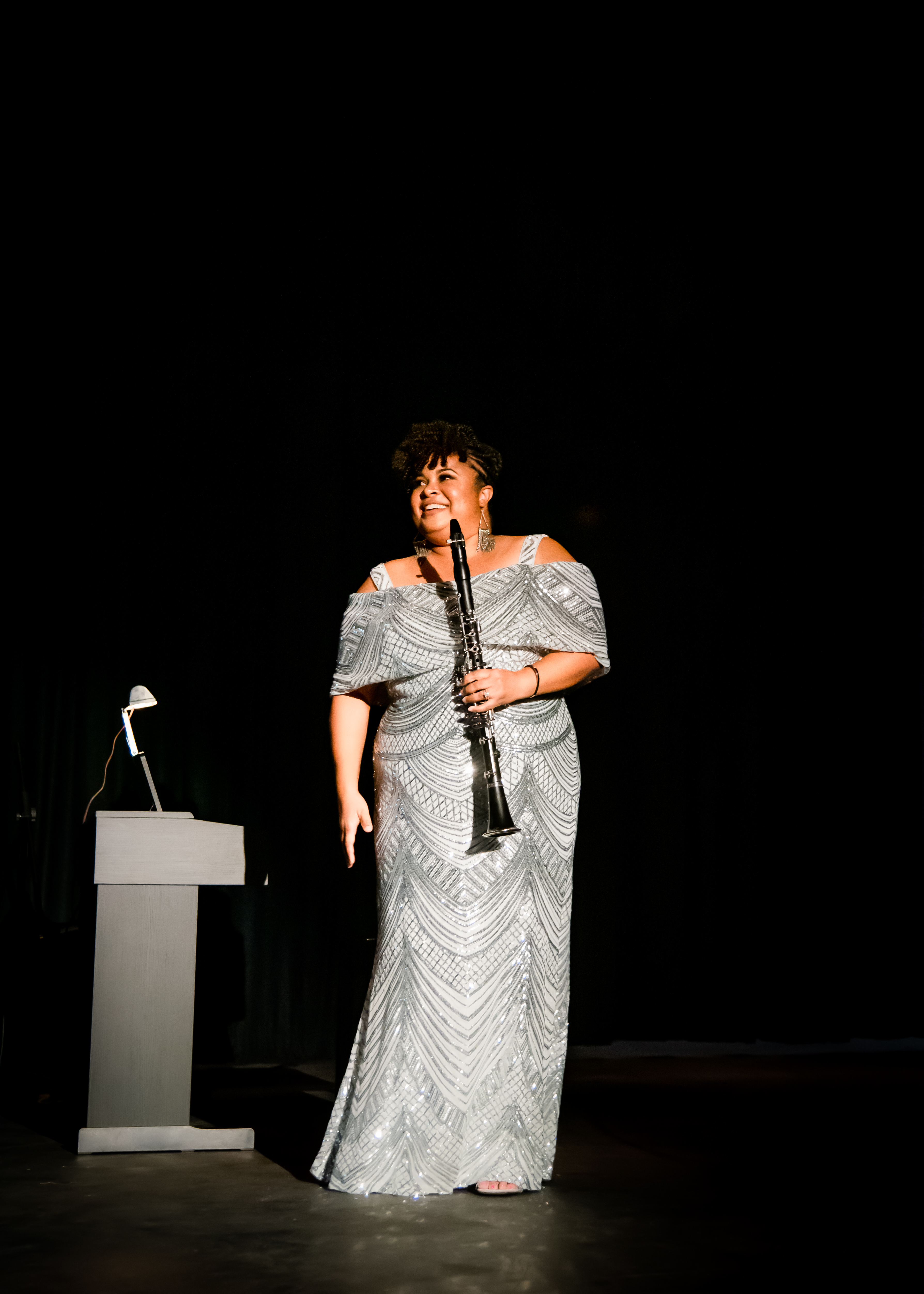 Portrait of Ms. Tiana Okafor, a young Black woman with short curly hair, wearing a sleek yellow dress, standing in front of a bookshelf. Her expression is thoughtful and inviting, suggesting expertise in personal development.