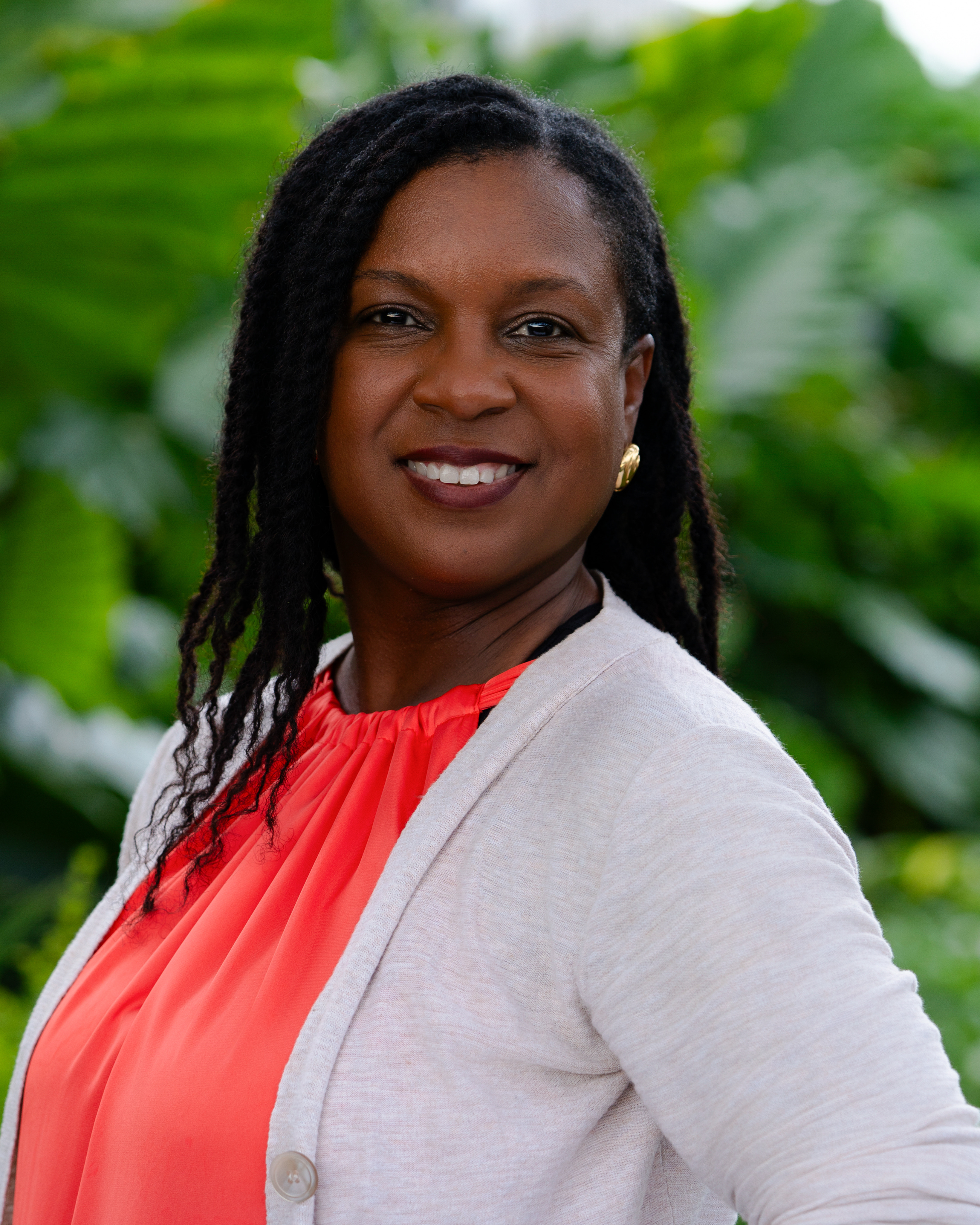 Portrait of Coach Maya Roberts, a Black woman in her 50s with silver-streaked locs, wearing a tailored black suit, seated in a modern chair. Her poised demeanor and gentle smile radiate wisdom and encouragement.