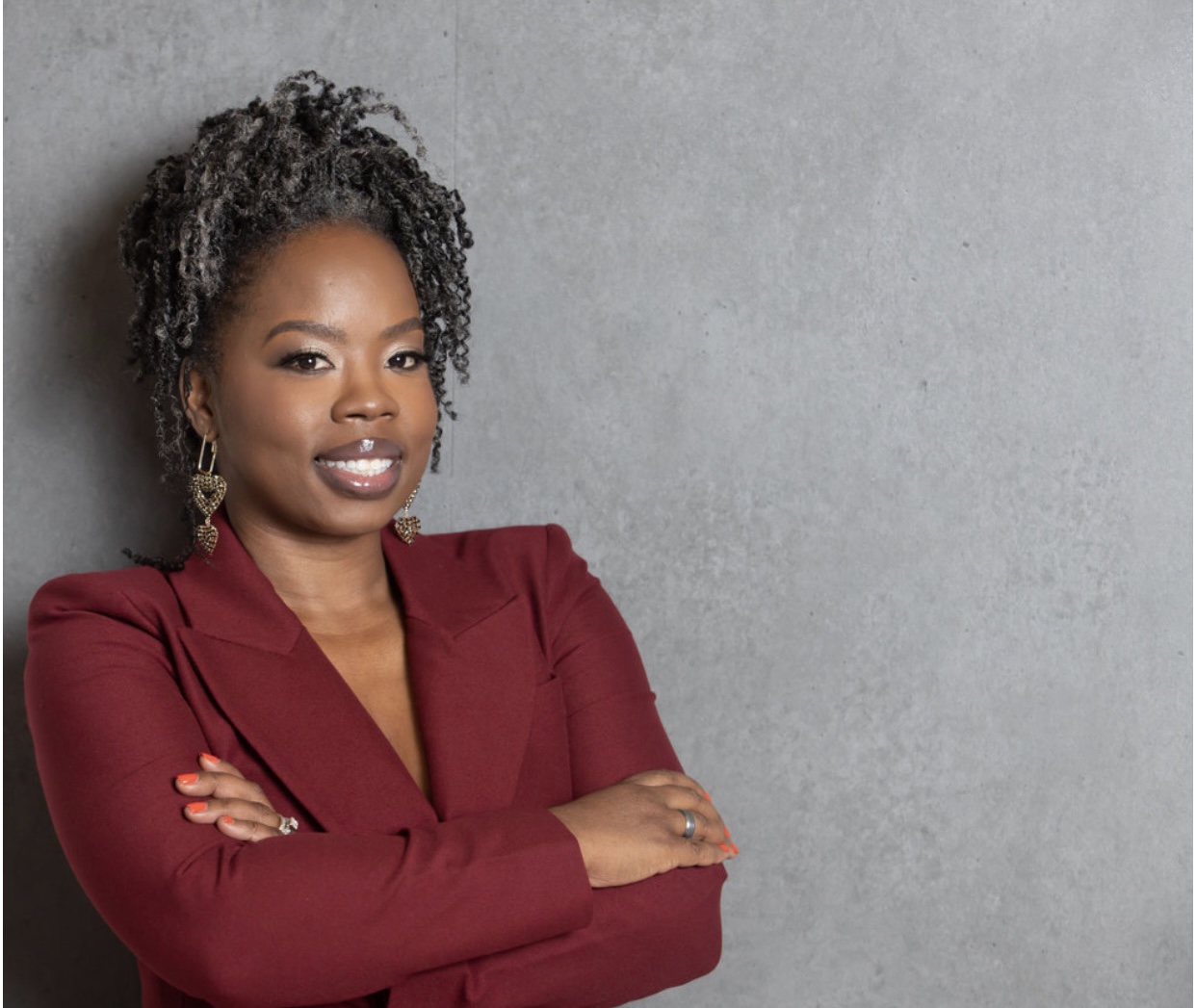 Portrait of Dr. Alicia James, a Black woman in her 40s with natural hair, wearing a vibrant patterned blazer, smiling warmly against a soft studio background. Her confident posture and direct gaze convey wisdom and approachability.