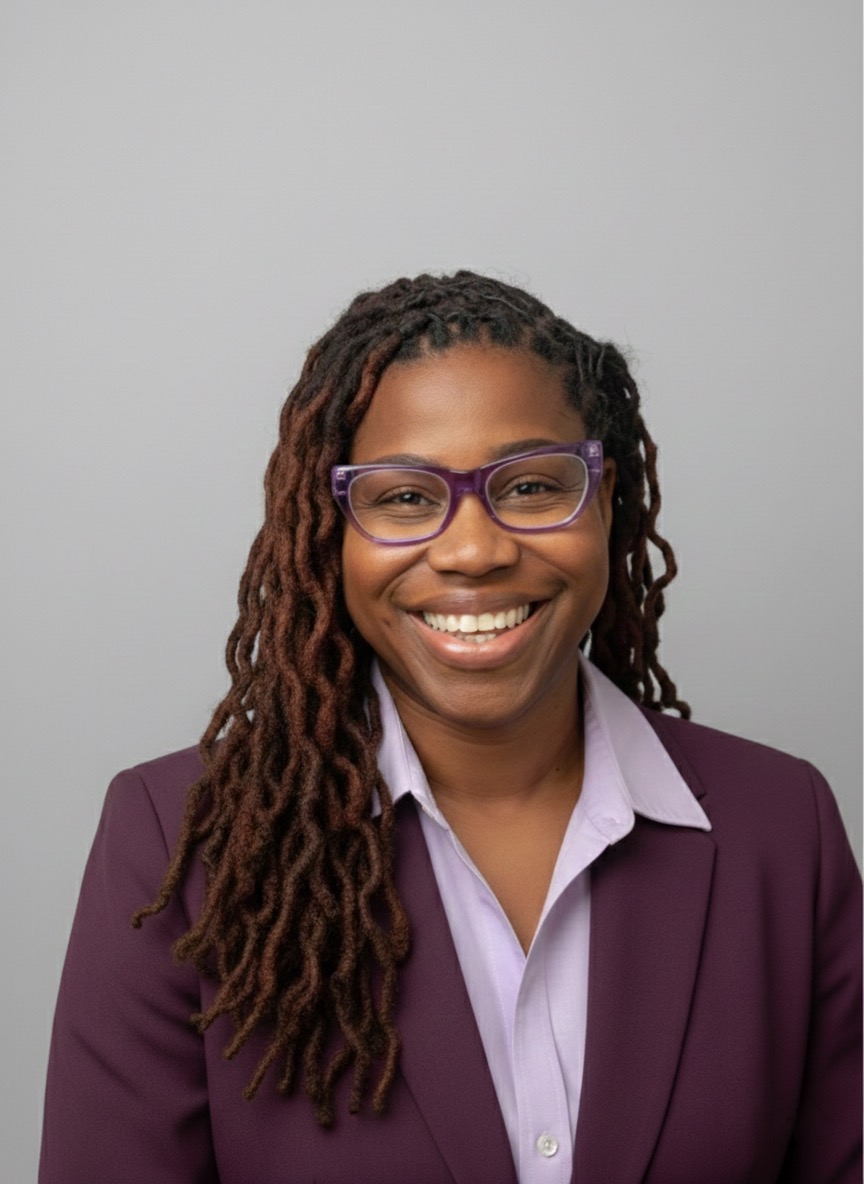 Portrait of Dr. Alicia James, a Black woman in her 40s with natural hair, wearing a vibrant patterned blazer, smiling warmly against a soft studio background. Her confident posture and direct gaze convey wisdom and approachability.