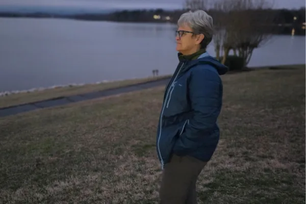 Claudette Paulin Eames standing by a lake at dusk, reflecting on grief, joy, and love seventeen years after the loss of her husband.