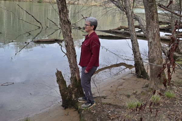 Claudette Eames standing by a still lake in the woods reflecting on the people who changed her life for good