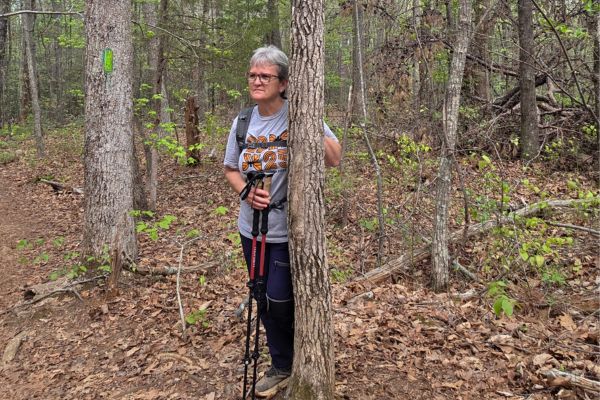 woman pausing on forest trail with hiking poles reflecting during a walk due to knee limitation