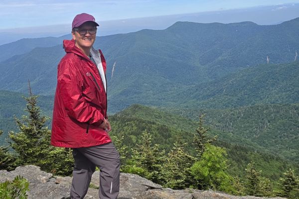 Claudette Eames standing on a rocky overlook near Mount Mitchell in North Carolina with layers of Blue Ridge Mountains stretching into the distance behind her.