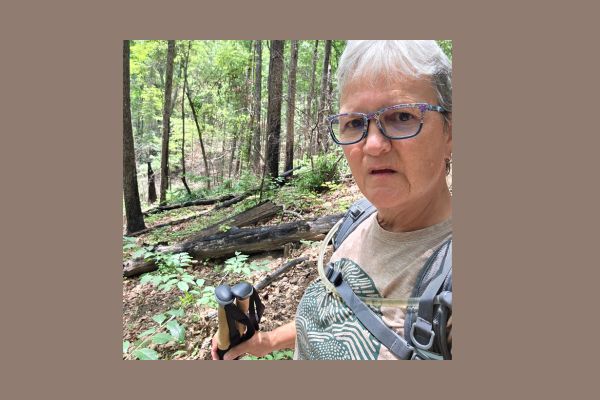 Claudette hiking on a wooded trail in South Carolina near trees scarred by a past wildfire, reflecting on solitude, resilience, and personal growth.